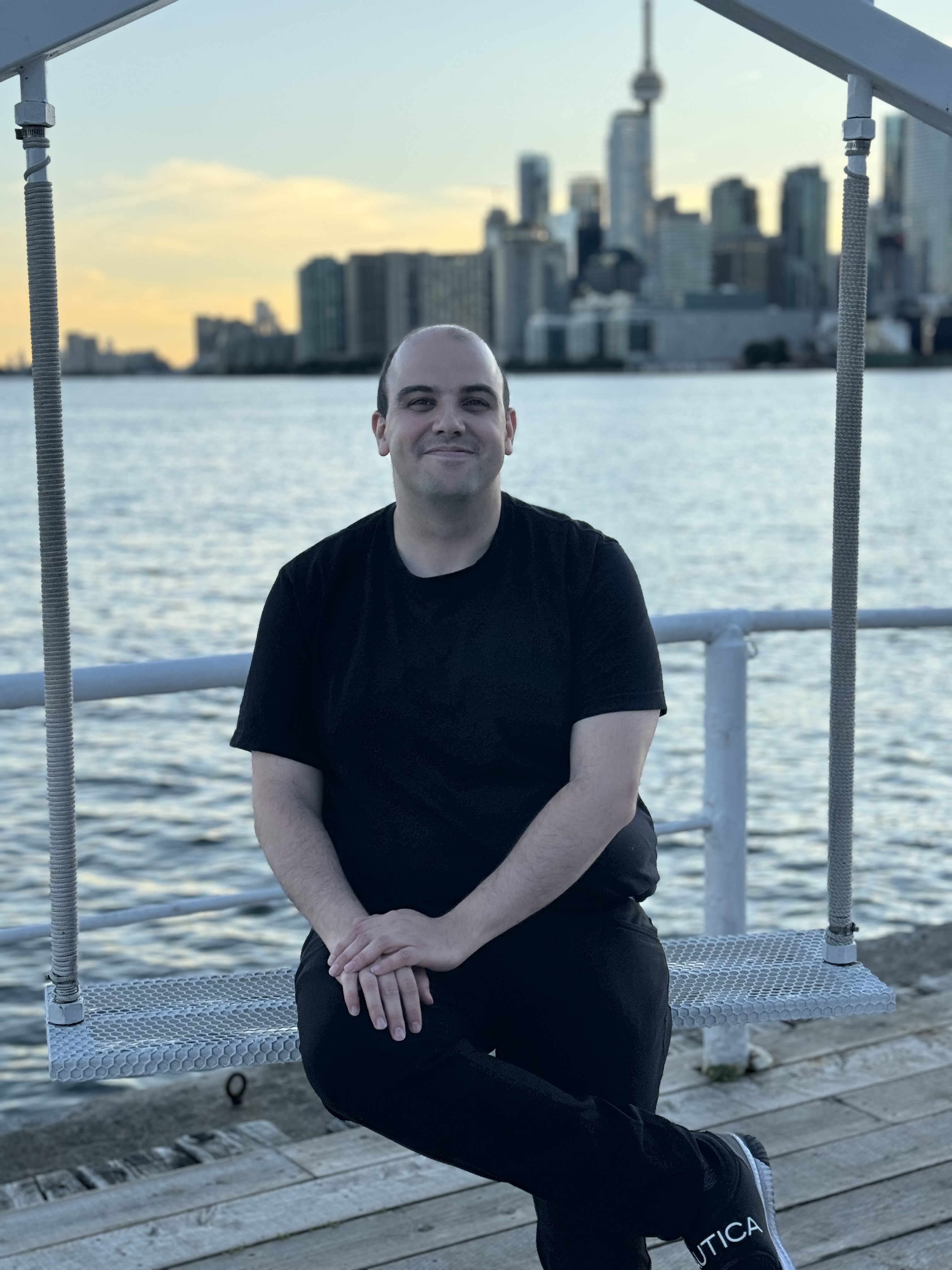 Or Grunebaum sitting on a metal swing with Toronto cityscape in the background